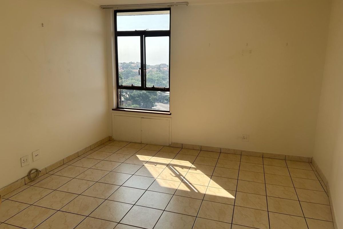 An empty bedroom featuring tiled flooring, a large window with natural light, and neutral wall finishes, ready for personalization.