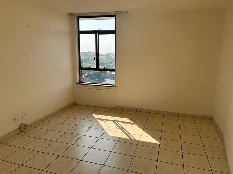 An empty bedroom featuring tiled flooring, a large window with natural light, and neutral wall finishes, ready for personalization.