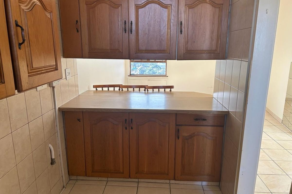 A dated kitchen area featuring traditional wooden cabinetry, laminate countertops, and ceramic tiling throughout.
