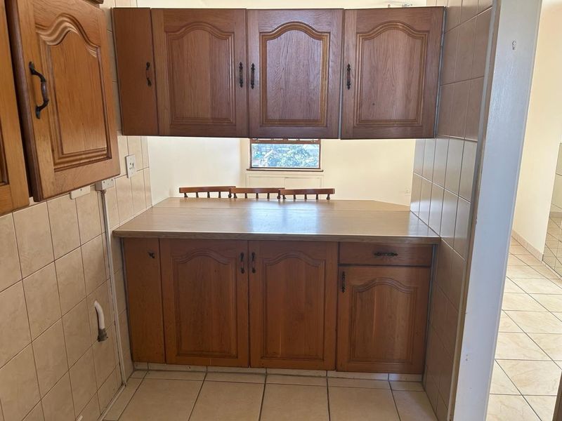 A dated kitchen area featuring traditional wooden cabinetry, laminate countertops, and ceramic tiling throughout.