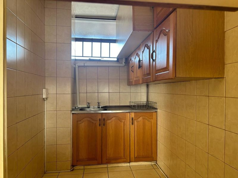 A compact scullery or utility area featuring tiled finishes, built-in wooden cabinetry, and a stainless steel sink with exposed plumbing.