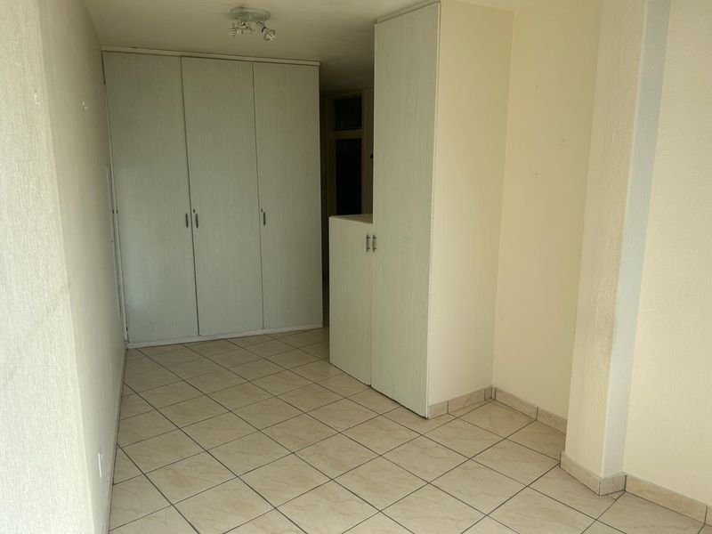 An empty bedroom featuring tiled flooring and built-in cupboards, offering a neutral space ready for personalization.