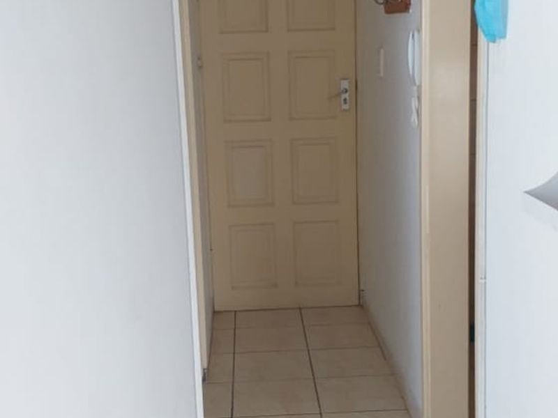 A functional hallway featuring neutral tiled flooring, a classic panelled door with a transom window, and simple overhead lighting.