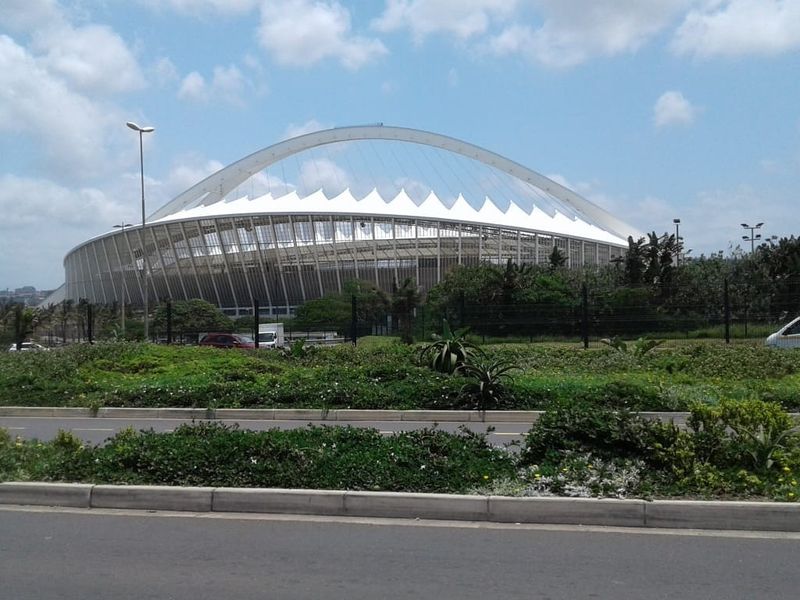 A clear view of the iconic stadium structure from the roadside, showcasing the prominent architectural arch and roof design.