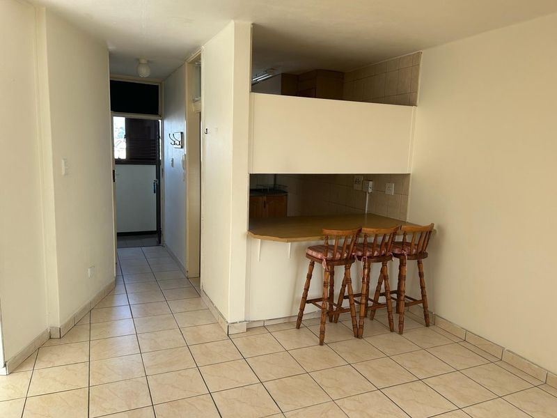 Open plan living area featuring a breakfast bar counter and tiled flooring, leading into a kitchen space with tiled backsplash.