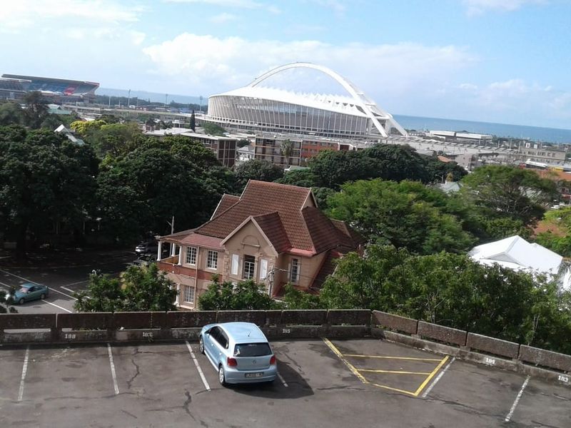 An elevated view overlooking the surrounding urban landscape, featuring a prominent stadium in the distance and a paved parking area in the foreground.