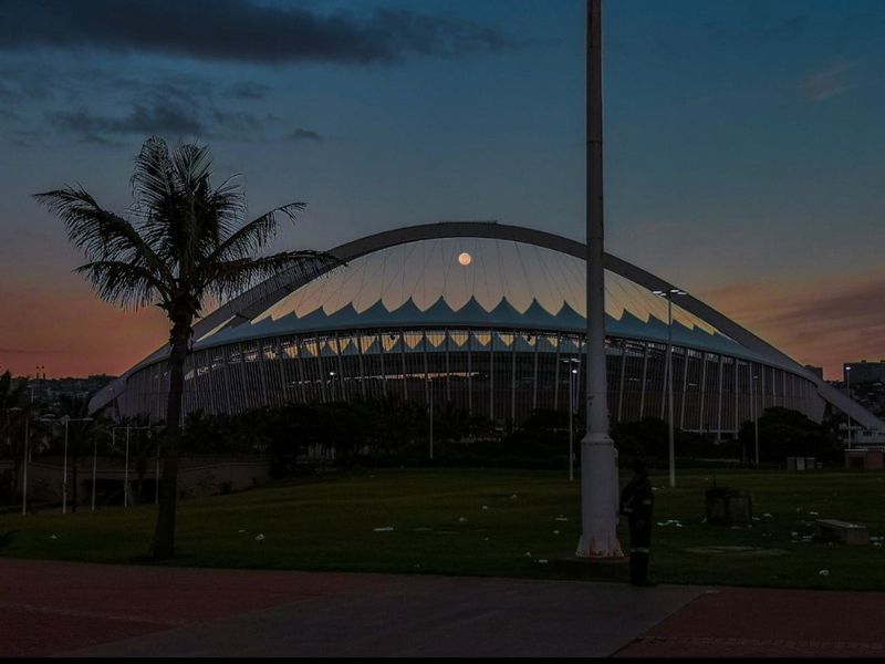 A scenic evening view of the Moses Mabhida Stadium in Durban, showcasing its iconic arch structure against a twilight sky.
