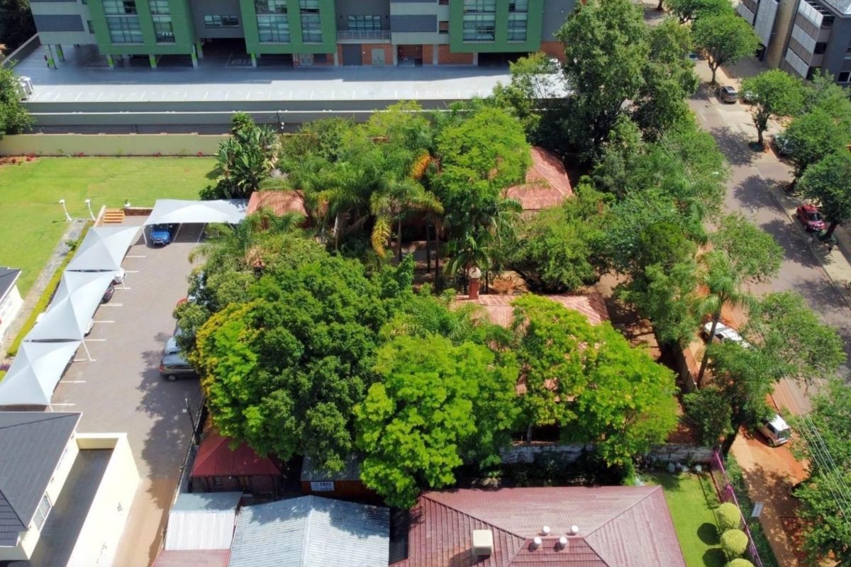Aerial view of the commercial property featuring a tiled roof building, mature trees, and a paved parking area with shade cloth carports.