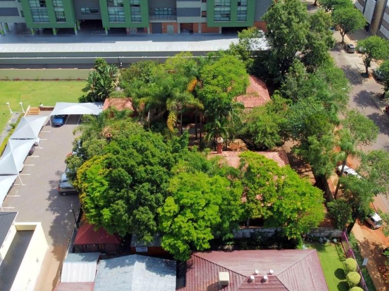 Aerial view of the commercial property featuring a tiled roof building, mature trees, and a paved parking area with shade cloth carports.