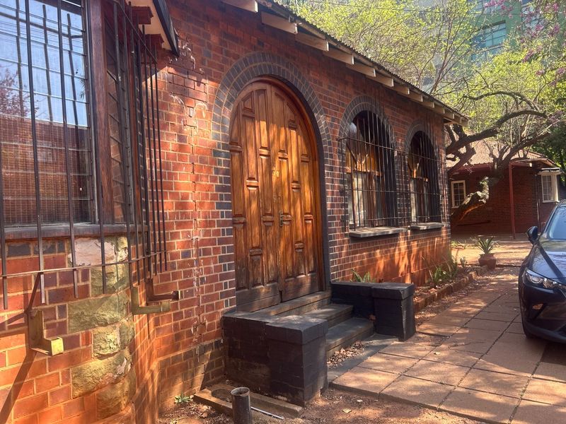 Front exterior view of a commercial building featuring classic red brick construction, arched wooden double doors, and security-barred windows along a paved walkway.
