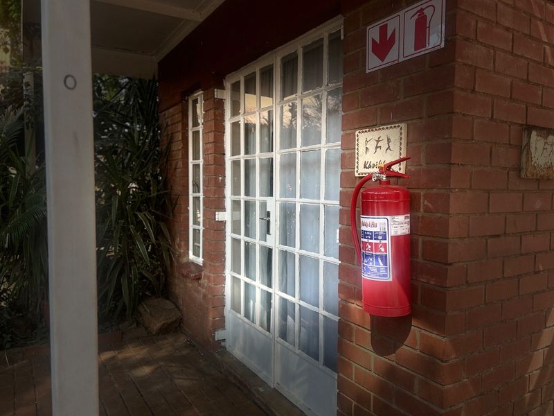 Exterior view of a commercial building entrance featuring a brick facade, white-framed french doors, and a mounted fire extinguisher.