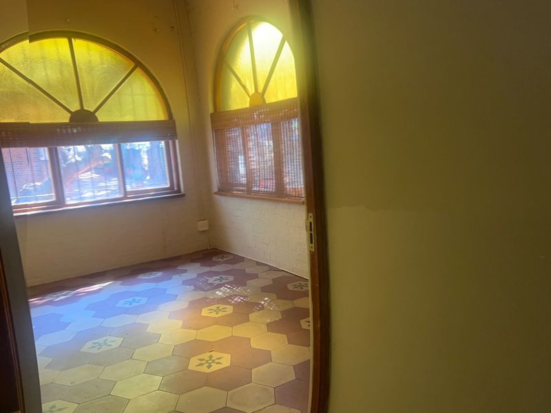 An empty office space featuring distinctive arched windows and patterned hexagonal floor tiles, offering a unique architectural character in need of refurbishment.