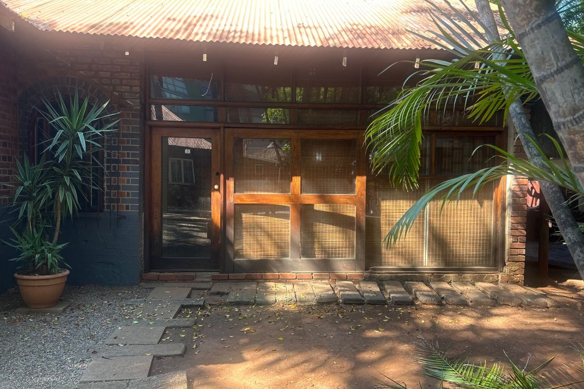 Rear exterior view of a commercial building featuring exposed brickwork, a corrugated metal roof, and timber-framed glass entrance doors with a stone paver path.