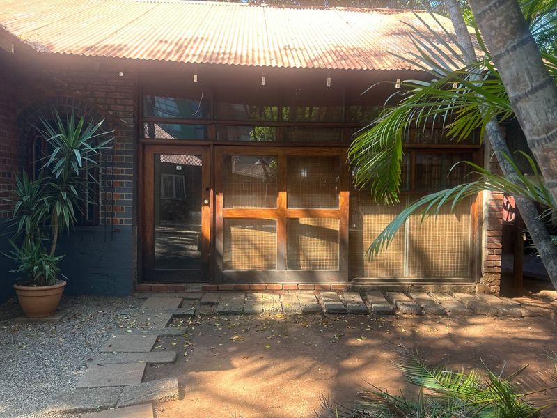 Rear exterior view of a commercial building featuring exposed brickwork, a corrugated metal roof, and timber-framed glass entrance doors with a stone paver path.