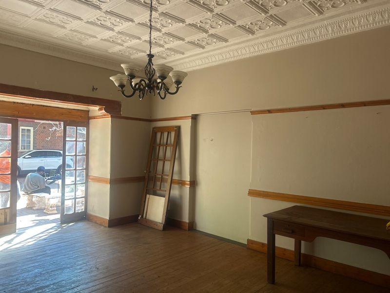 Spacious living area featuring a decorative pressed metal ceiling, timber flooring, and a classic chandelier, offering a blank canvas for renovation.