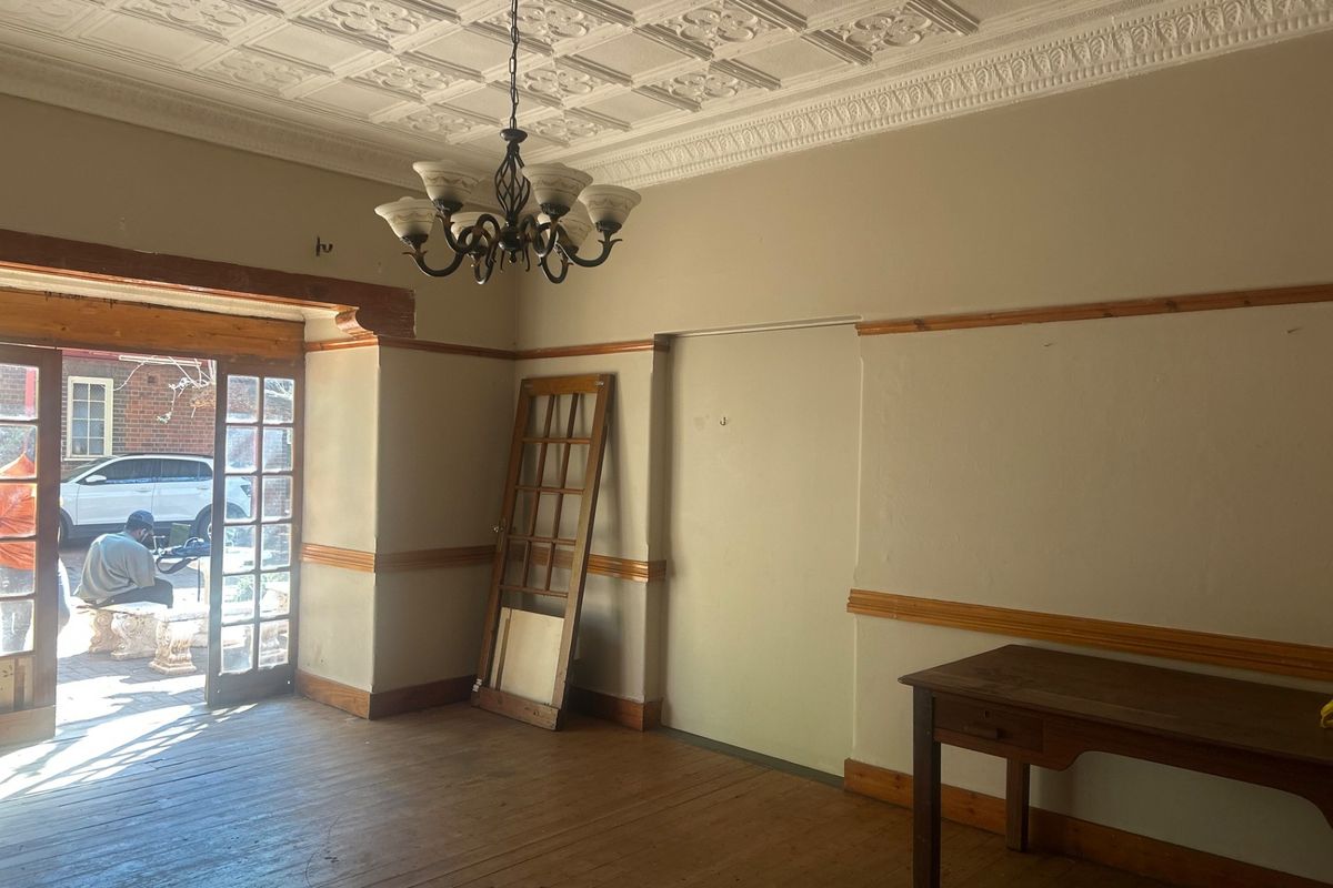Spacious living area featuring a decorative pressed metal ceiling, timber flooring, and a classic chandelier, offering a blank canvas for renovation.