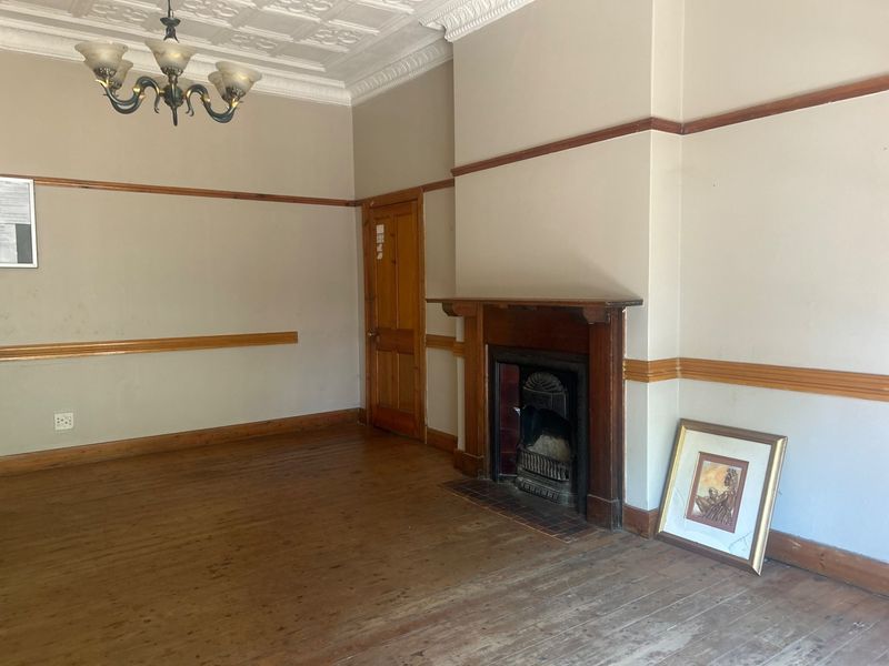 A vacant living room featuring original timber flooring, a traditional fireplace with a timber mantelpiece, and decorative ceiling detailing.