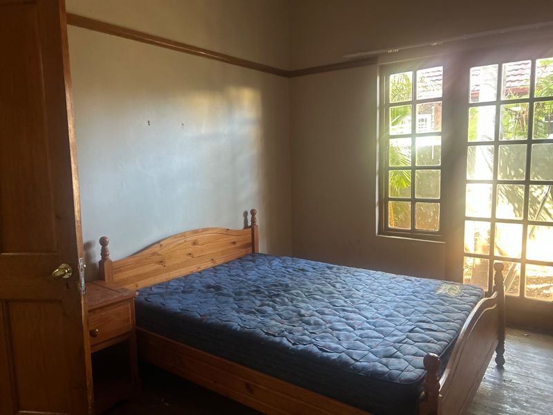 A bedroom featuring timber door and window frames with natural light, requiring cosmetic updates to the walls and flooring.