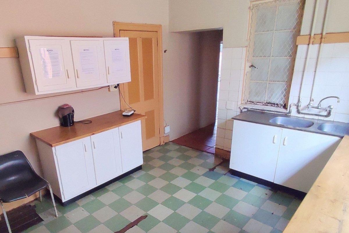 A dated kitchen area featuring built-in cabinetry, a stainless steel sink, and checkered tile flooring, requiring cosmetic updates to modernize the space.
