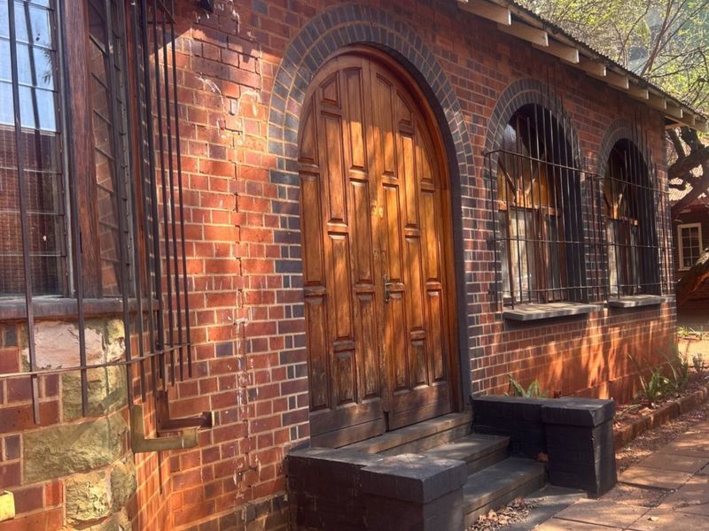 A commercial building exterior featuring classic red brick construction, arched wooden double doors, and arched windows with security bars.
