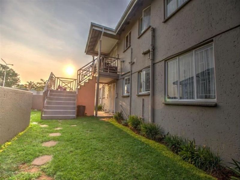 Rear exterior view of the townhouse featuring a grass garden, paved stepping stones, and an external staircase leading to an upper-level balcony.