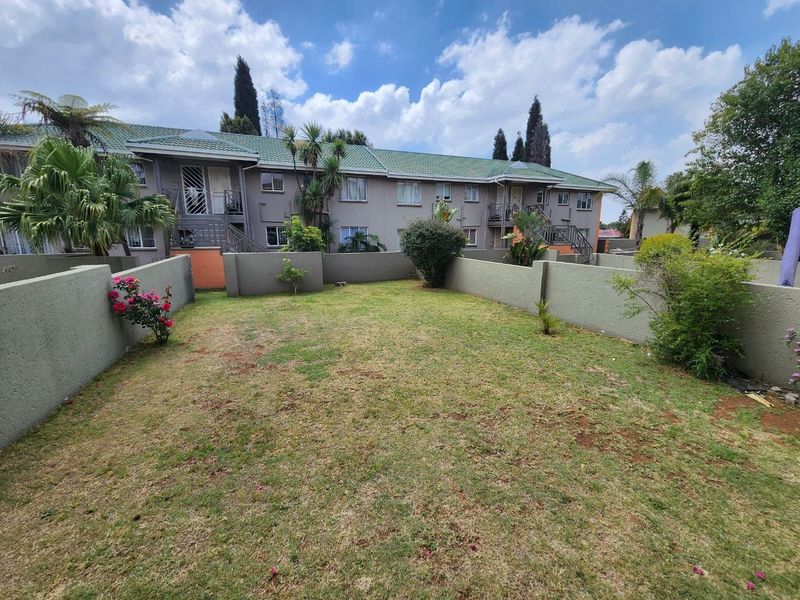 A private rear garden area featuring a lawn, boundary walls, and a view of the townhouse complex exterior with staircases.