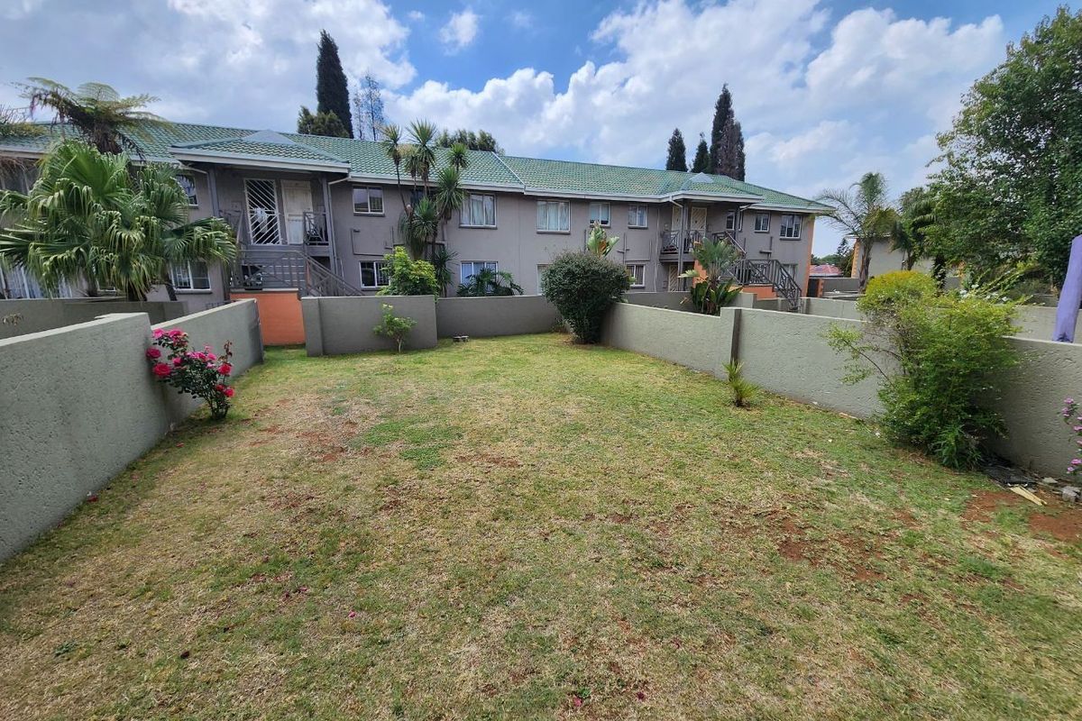A private rear garden area featuring a lawn, boundary walls, and a view of the townhouse complex exterior with staircases.