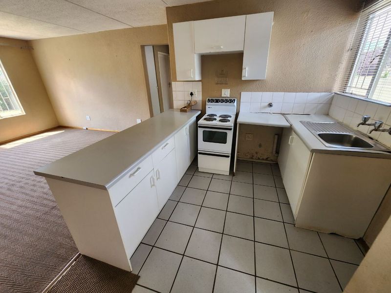 Open-plan kitchen area featuring white cabinetry, a freestanding stove, and tiled flooring, adjacent to a carpeted living space.