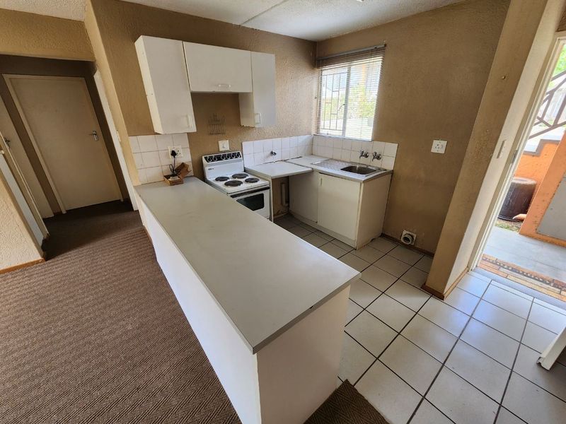 A compact, dated kitchen featuring a breakfast bar, electric stove, and basic cabinetry, offering potential for a modern renovation.