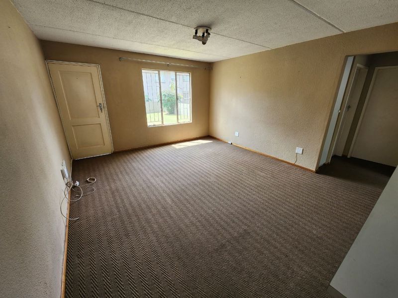 An empty living room featuring textured walls, carpet flooring, and security bars on the window, offering a blank canvas for renovation.