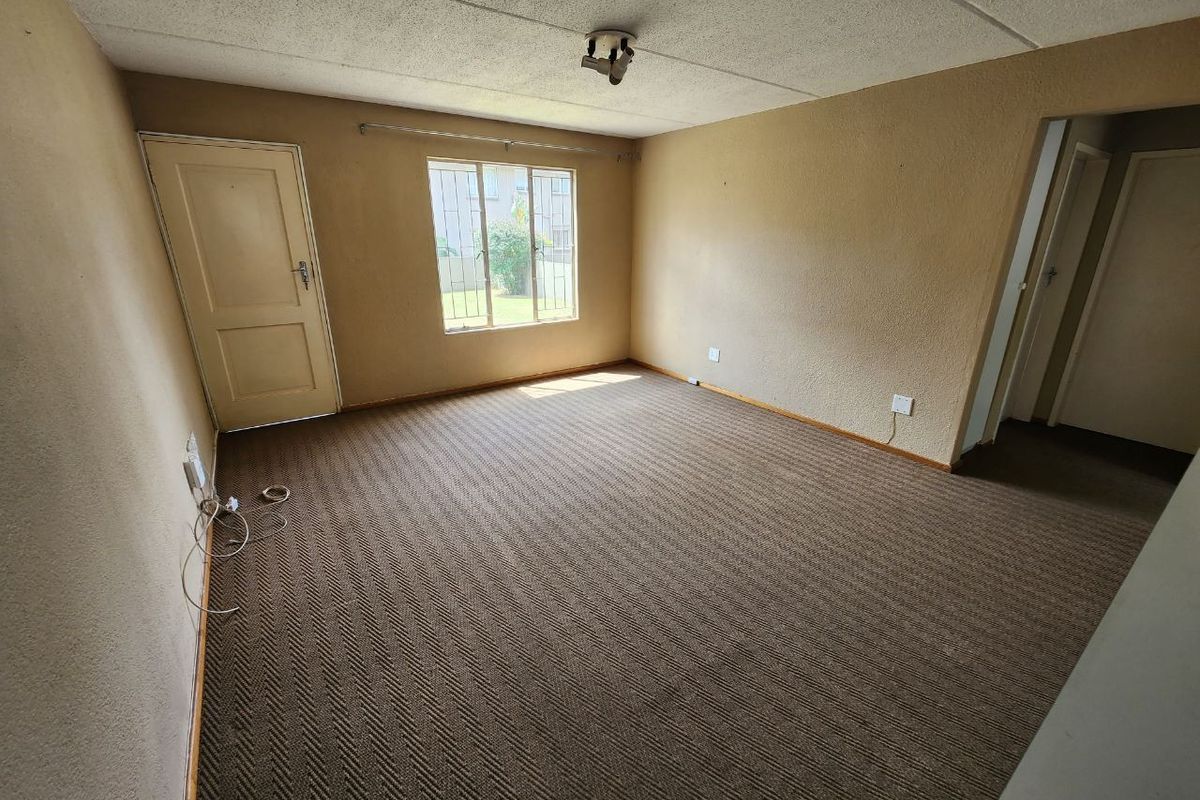 An empty living room featuring textured walls, carpet flooring, and security bars on the window, offering a blank canvas for renovation.
