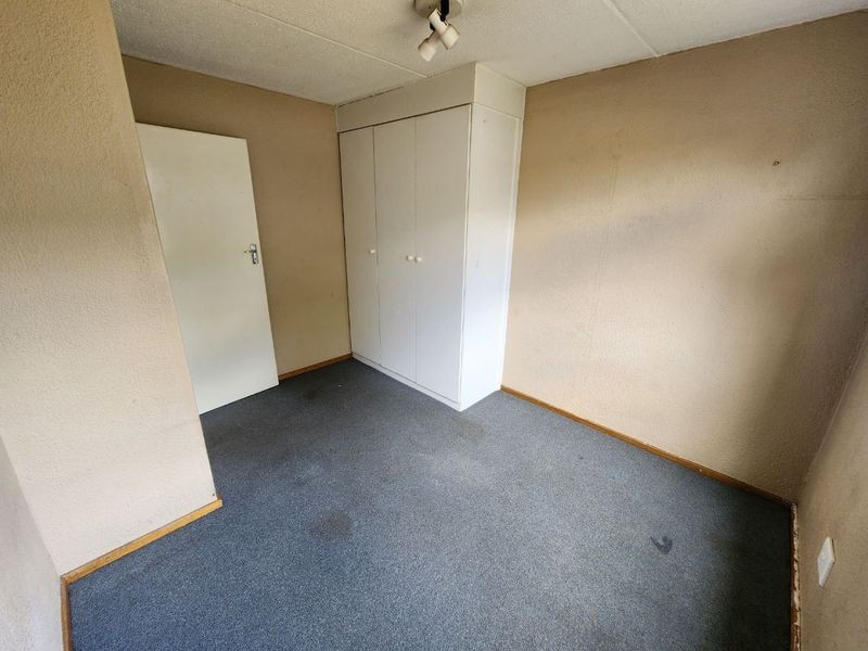 An empty bedroom featuring built-in wardrobes, carpeted flooring, and a neutral color palette, ready for renovation or staging.