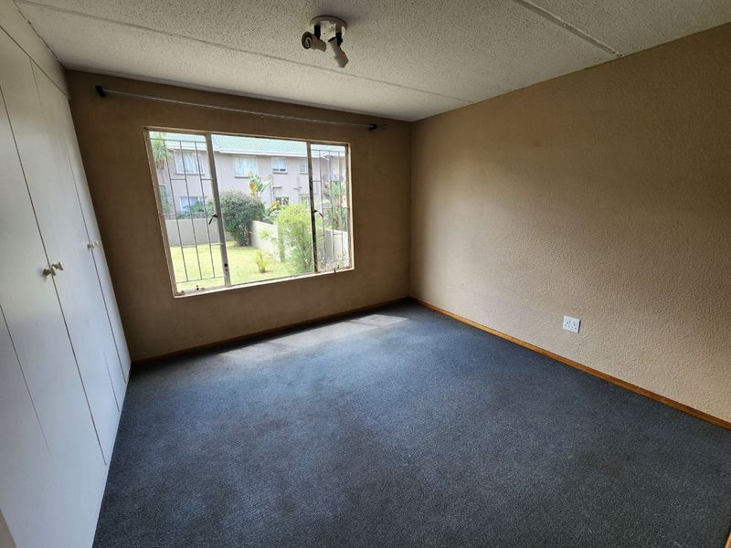 A vacant bedroom featuring built-in cupboards, carpeted flooring, and security bars on the window, offering a blank canvas for renovation.