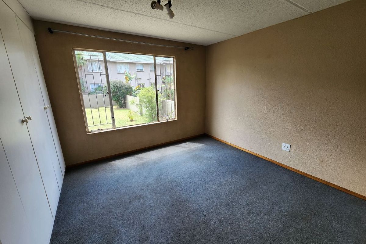 A vacant bedroom featuring built-in cupboards, carpeted flooring, and security bars on the window, offering a blank canvas for renovation.