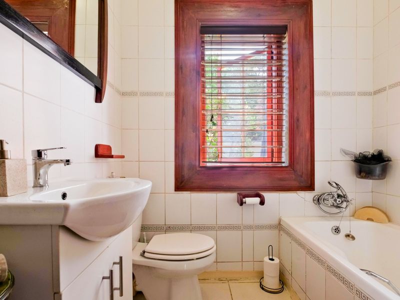A functional bathroom featuring a vanity basin, toilet, and bathtub with tiled walls and a timber-framed window.