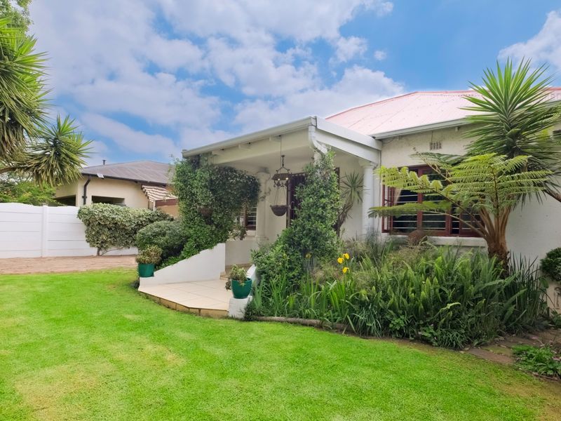 Front view of a well-maintained house featuring a covered patio, established garden, and secure boundary walling.