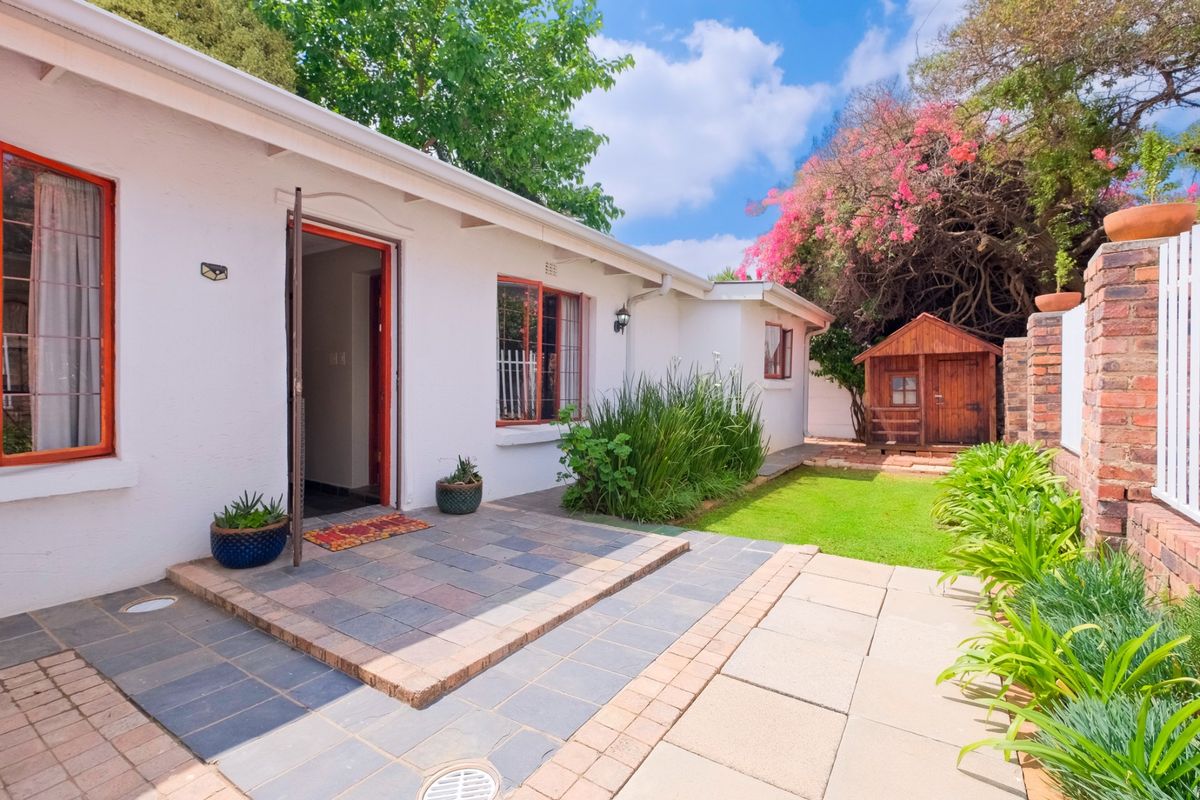 A well-maintained rear garden featuring a tiled patio, brick paving, a small lawn, and a charming wooden garden shed.