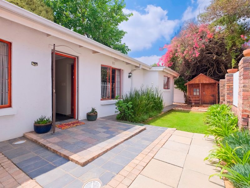 A well-maintained rear garden featuring a tiled patio, brick paving, a small lawn, and a charming wooden garden shed.