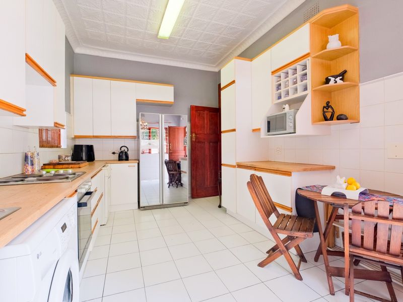 A functional kitchen featuring white cabinetry, timber countertops, tiled flooring, and a distinctive pressed metal ceiling, offering a practical layout with integrated appliances.