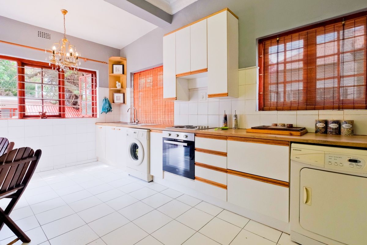 A functional kitchen featuring white cabinetry with wood trim, tiled flooring, a built-in oven and hob, and ample counter space.