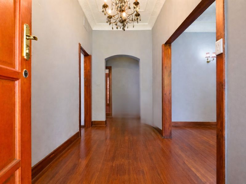A spacious hallway featuring polished hardwood flooring, classic timber door frames, and an ornate ceiling rose, providing a warm and inviting transition between rooms.