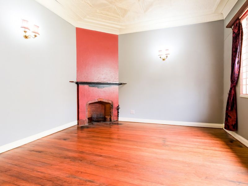 A bright, empty living room featuring original hardwood flooring, a corner fireplace, and decorative ceiling molding.