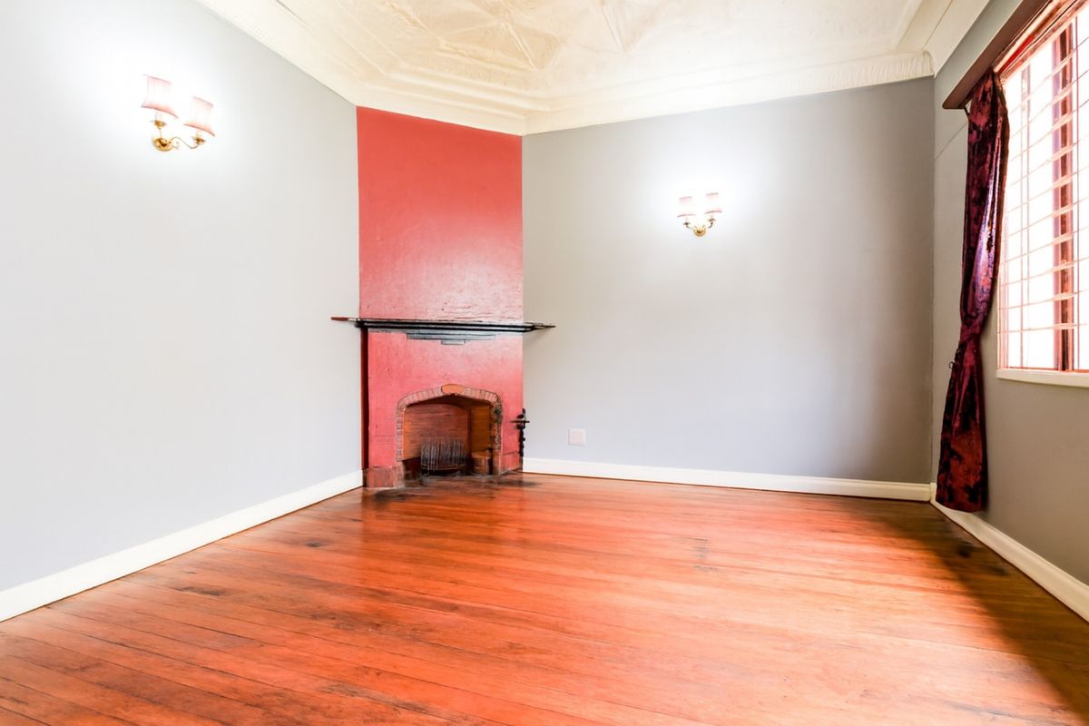 A bright, empty living room featuring original hardwood flooring, a corner fireplace, and decorative ceiling molding.