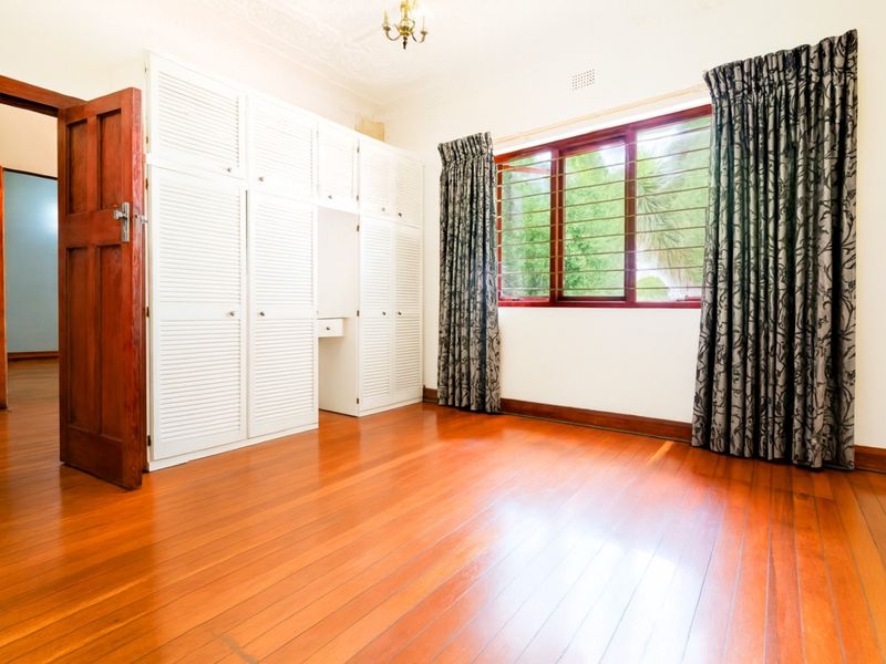 Spacious bedroom featuring polished hardwood flooring, extensive built-in white cabinetry, and large windows with security bars, offering a bright and classic aesthetic.