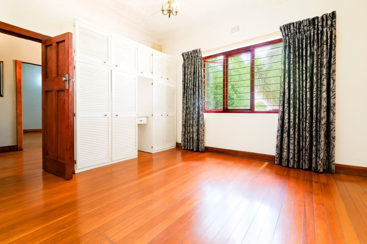 Spacious bedroom featuring polished hardwood flooring, extensive built-in white cabinetry, and large windows with security bars, offering a bright and classic aesthetic.