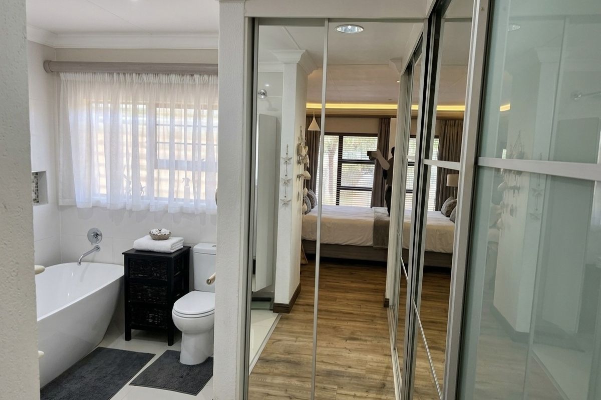 Modern bathroom featuring a freestanding bathtub and toilet, adjacent to a bedroom area with built-in mirrored sliding wardrobes and wood-look flooring.