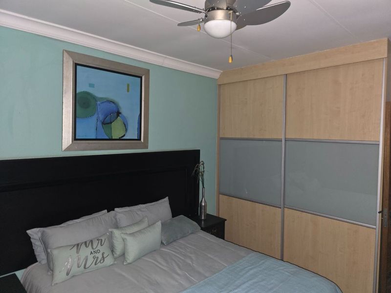 A well-maintained bedroom featuring a large built-in sliding door wardrobe, ceiling fan, and decorative coved cornice.