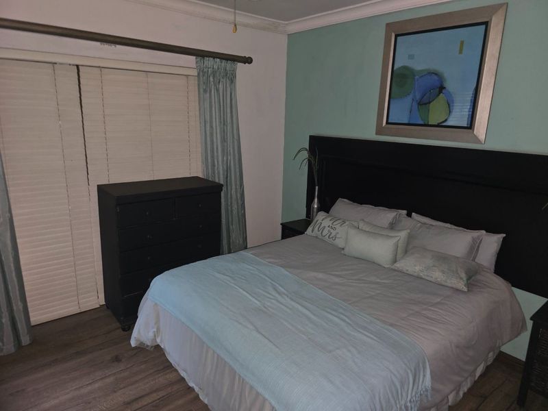 A bedroom featuring laminate flooring, a sliding door with venetian blinds, and a decorative ceiling cornice.