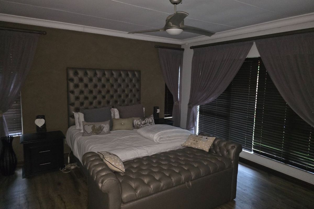 A well-maintained bedroom featuring laminate flooring, a ceiling fan, and dark venetian blinds, offering a comfortable and private sleeping space.