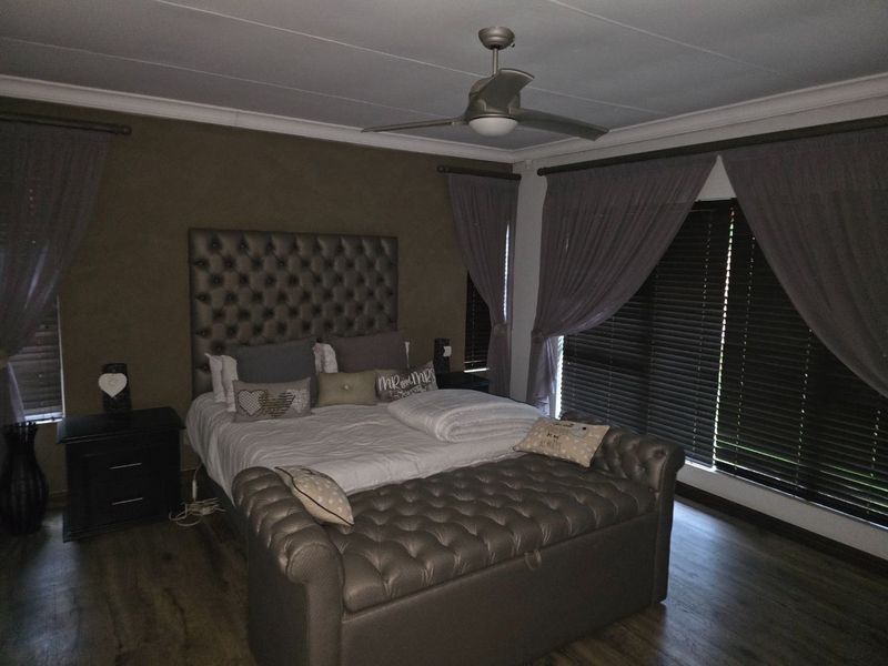 A well-maintained bedroom featuring laminate flooring, a ceiling fan, and dark venetian blinds, offering a comfortable and private sleeping space.
